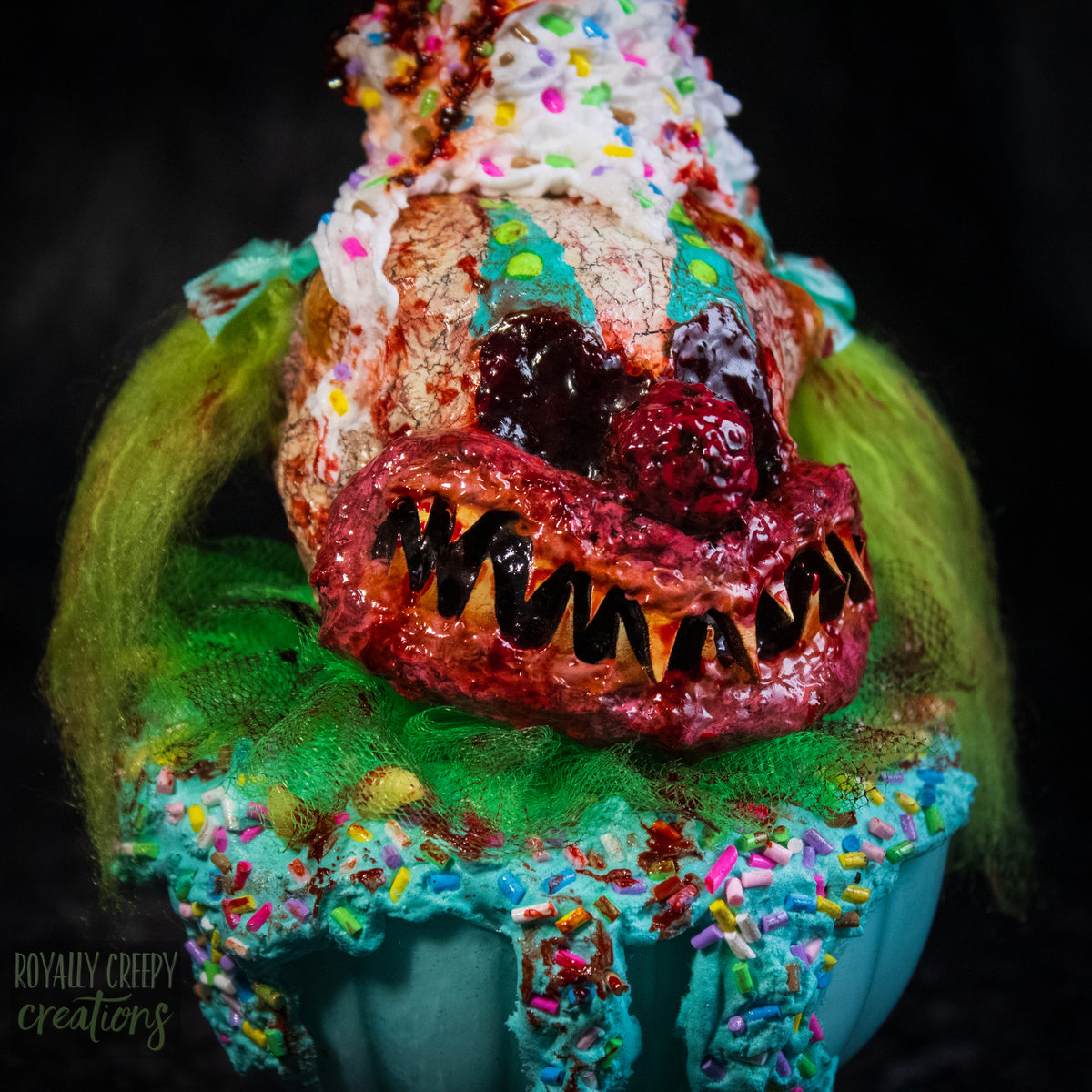 A close-up of a highly detailed sculpture of a horror clown head staged like an ice cream sundae. The clown head is overflowing with whipped cream and ice cream and is sitting in a glass dessert bowl.