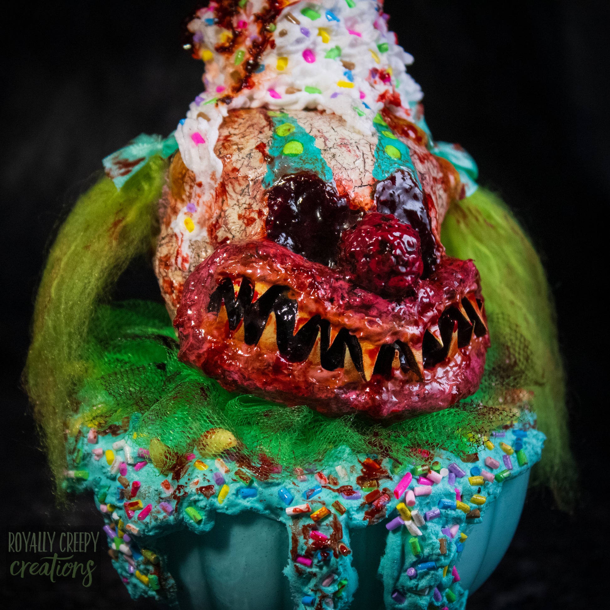 A close-up of a highly detailed sculpture of a horror clown head staged like an ice cream sundae. The clown head is overflowing with whipped cream and ice cream and is sitting in a glass dessert bowl.