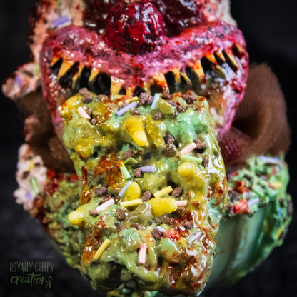 Close-up of a  highly detailed sculpture of a horror clown head staged like an ice cream sundae. The clown head is overflowing with whipped cream and ice cream and is sitting in a glass dessert bowl.