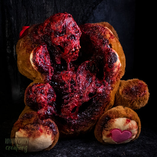 A horror-themed plush teddy bear that is split down the middle and a gory bloody skeleton is emerging from it's opening.