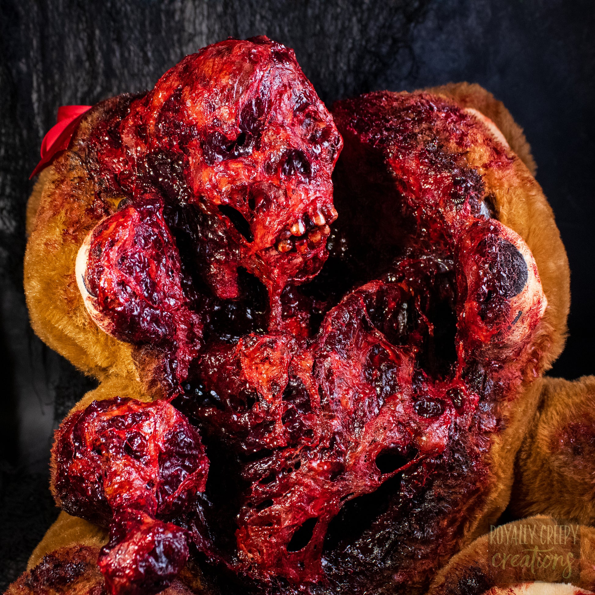 A close-up of a horror-themed plush teddy bear that is split down the middle and a gory bloody skeleton is emerging from it's opening.