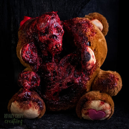 A horror-themed plush teddy bear that is split down the middle and a gory bloody skeleton is emerging from it's opening.