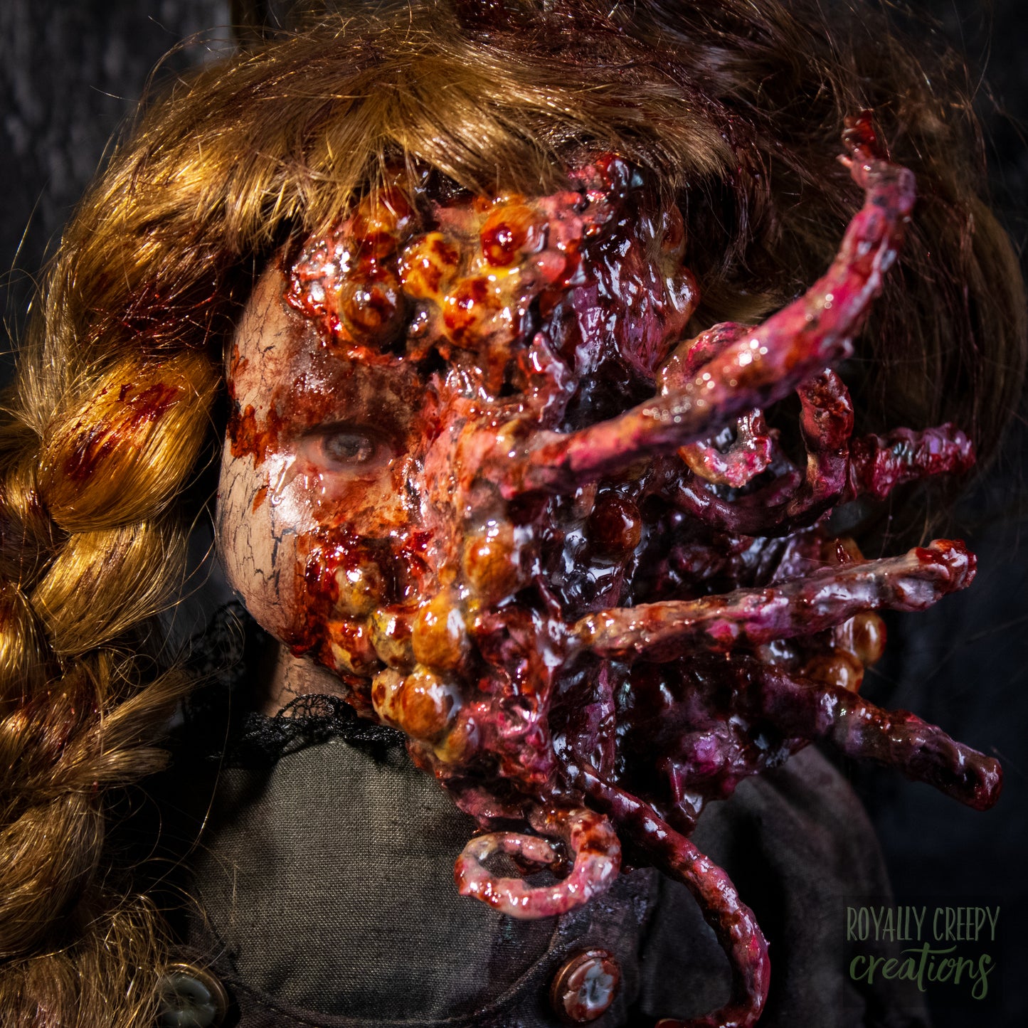 A close-up of a creepy horror doll, with long golden-brown hair and a grotesque red-orange fleshy appendage replacing half the face, against a dark textured backdrop. 