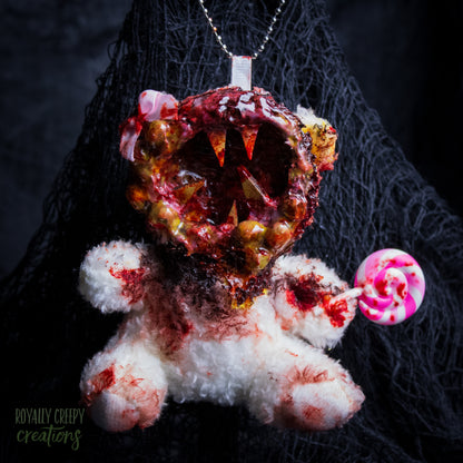 A horror-themed plush bear keychain with a bloody, gory mouth design, fuzzy body, and lollipop accessory, shown against a black netted backdrop.