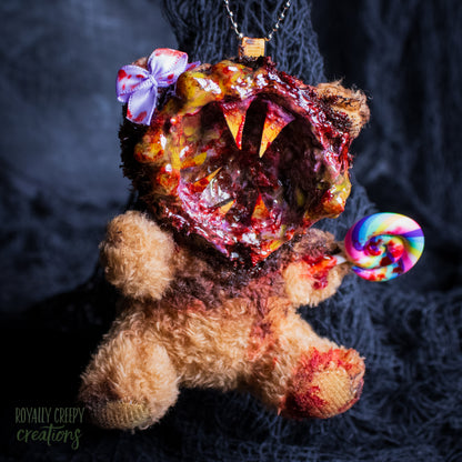 A horror-themed plush bear keychain with a bloody, gory mouth design, fuzzy body, and lollipop accessory, shown against a black netted backdrop.