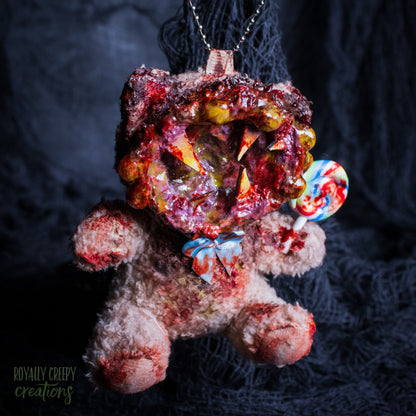 A horror-themed plush bear keychain with a bloody, gory mouth design, fuzzy body, and lollipop accessory, shown against a black netted backdrop.
