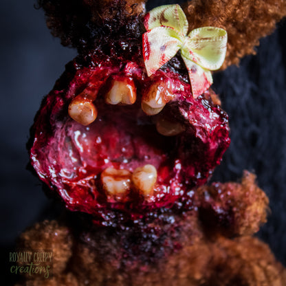 A close-up of a horror-themed plush bunny keychain with a bloody, gory mouth with human teeth taking over the whole face, fuzzy body, and wearing a bow.