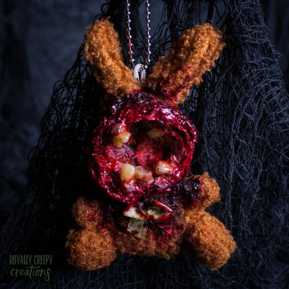 A horror-themed plush bunny keychain with a bloody, gory mouth with human teeth taking over the whole face, fuzzy body, and wearing a bow.