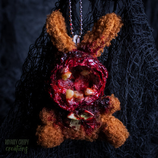 A horror-themed plush bunny keychain with a bloody, gory mouth with human teeth taking over the whole face, fuzzy body, and wearing a bow.