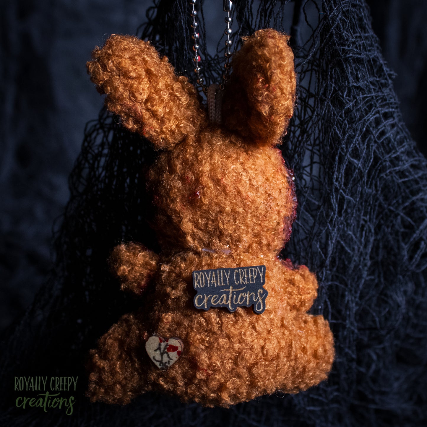 A back view of a plush bunny keychain with a 'royally creepy creations' patch