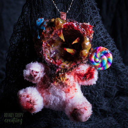 A horror-themed plush bear keychain with a bloody, gory mouth design, fuzzy body, and lollipop accessory, shown against a black netted backdrop.