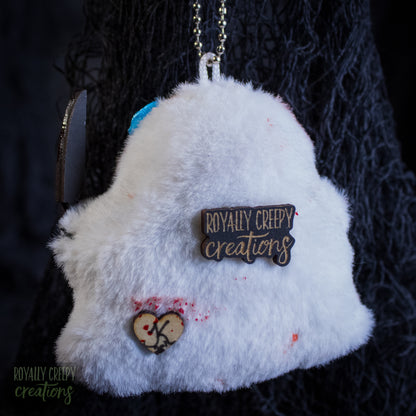 The back of a grotesque plush ghost keychain holding a fake knife.