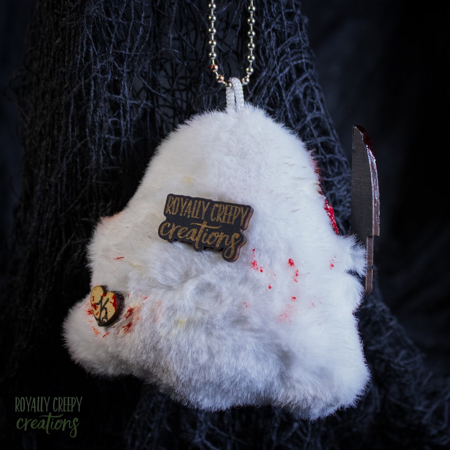 The back of a grotesque plush ghost keychain holding a fake knife.