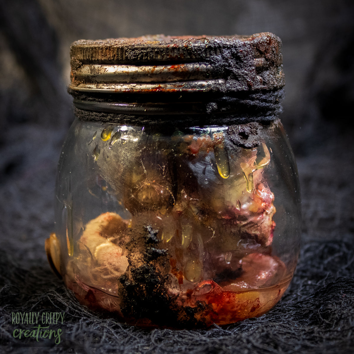 A creepy specimen prop of a severed doll head inside a dirty, rusted glass jar with a dark lid and rope, set against a dark textured background.