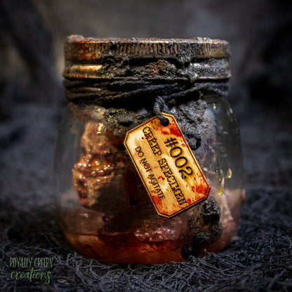 A creepy specimen prop of a severed doll head inside a dirty, rusted glass jar with a dark lid and rope, set against a dark textured background.
