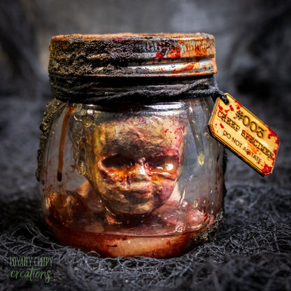 A creepy specimen prop of a severed doll head inside a dirty, rusted glass jar with a dark lid and rope, set against a dark textured background.