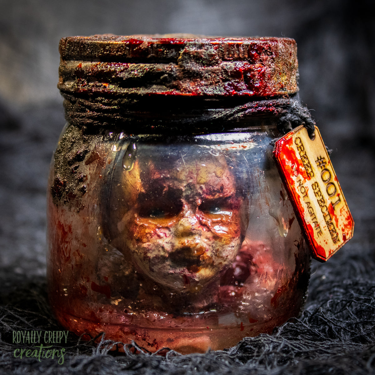 A creepy specimen prop of a severed doll head inside a dirty, rusted glass jar with a dark lid and rope, set against a dark textured background.