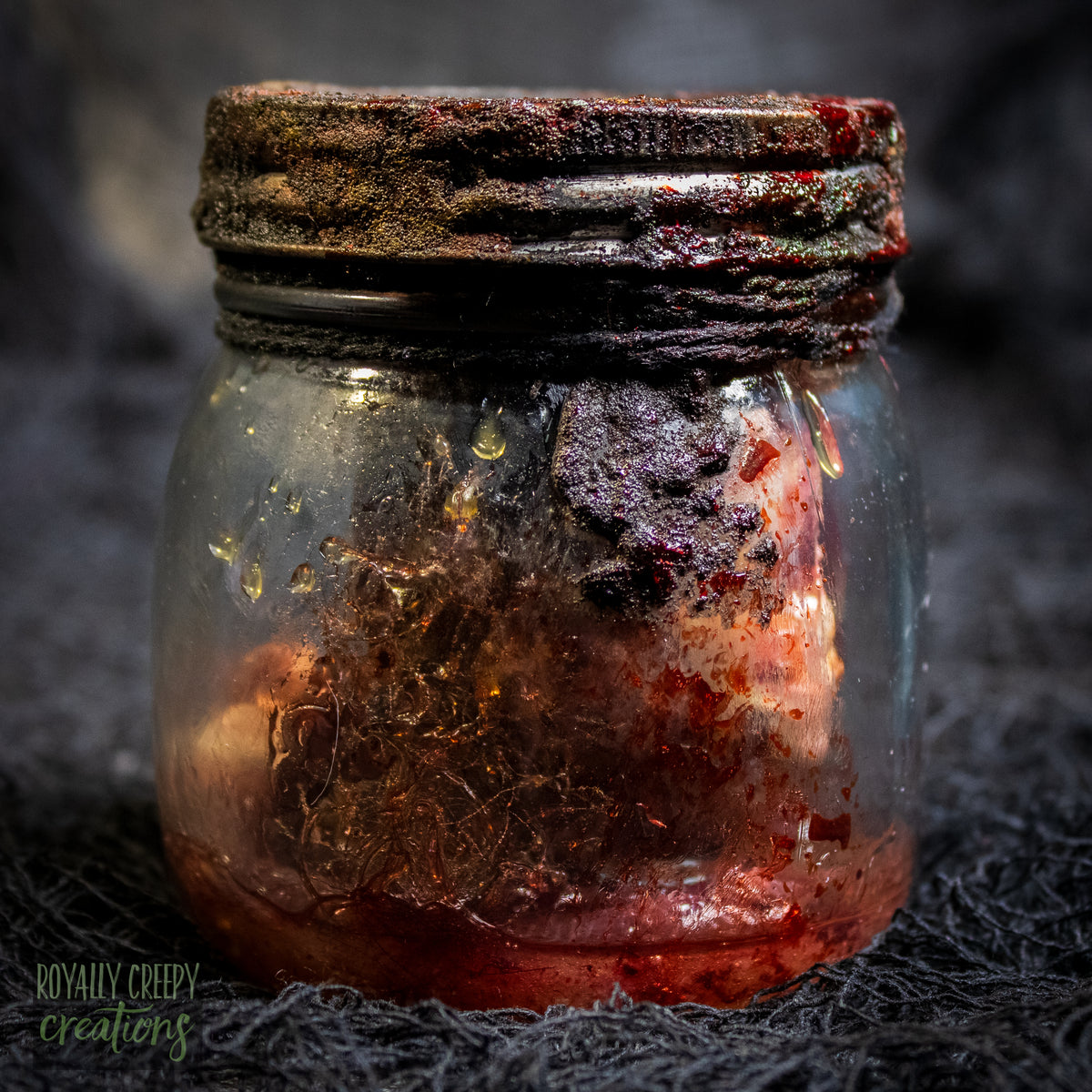 A creepy specimen prop of a severed doll head inside a dirty, rusted glass jar with a dark lid and rope, set against a dark textured background.