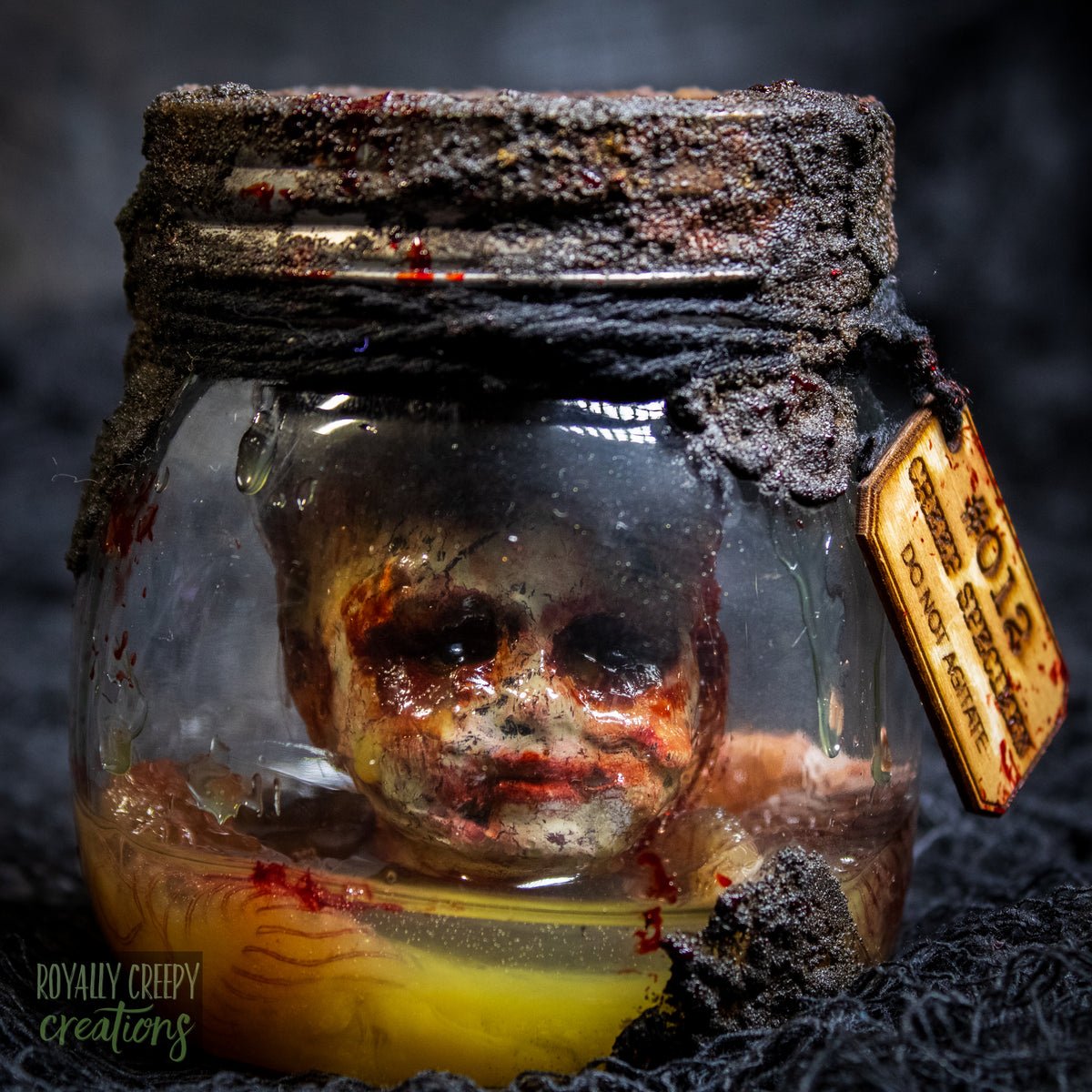 A creepy specimen prop of a severed doll head inside a dirty, rusted glass jar with a dark lid and rope, set against a dark textured background.