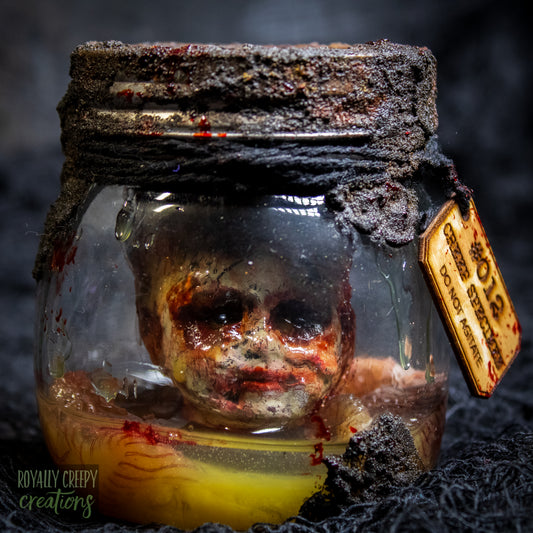 A creepy specimen prop of a severed doll head inside a dirty, rusted glass jar with a dark lid and rope, set against a dark textured background.