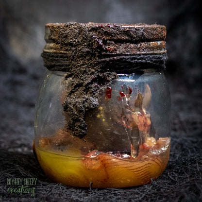 A creepy specimen prop of a severed doll head inside a dirty, rusted glass jar with a dark lid and rope, set against a dark textured background.