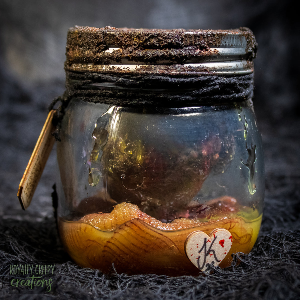 A creepy specimen prop of a severed doll head inside a dirty, rusted glass jar with a dark lid and rope, set against a dark textured background.