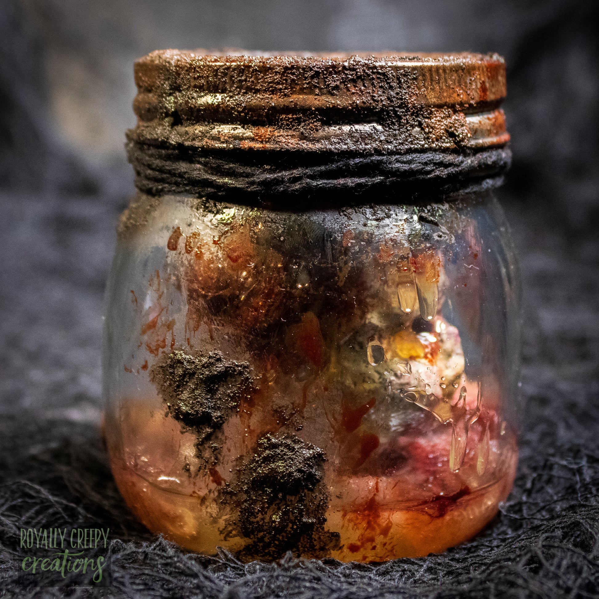 A creepy specimen prop of a severed doll head inside a dirty, rusted glass jar with a dark lid and rope, set against a dark textured background.