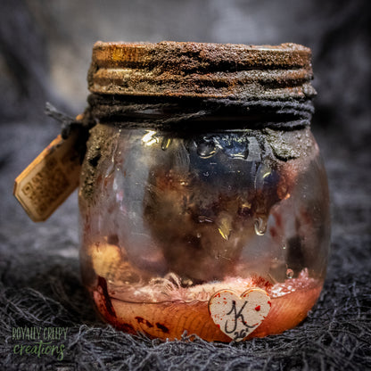 A creepy specimen prop of a severed doll head inside a dirty, rusted glass jar with a dark lid and rope, set against a dark textured background.
