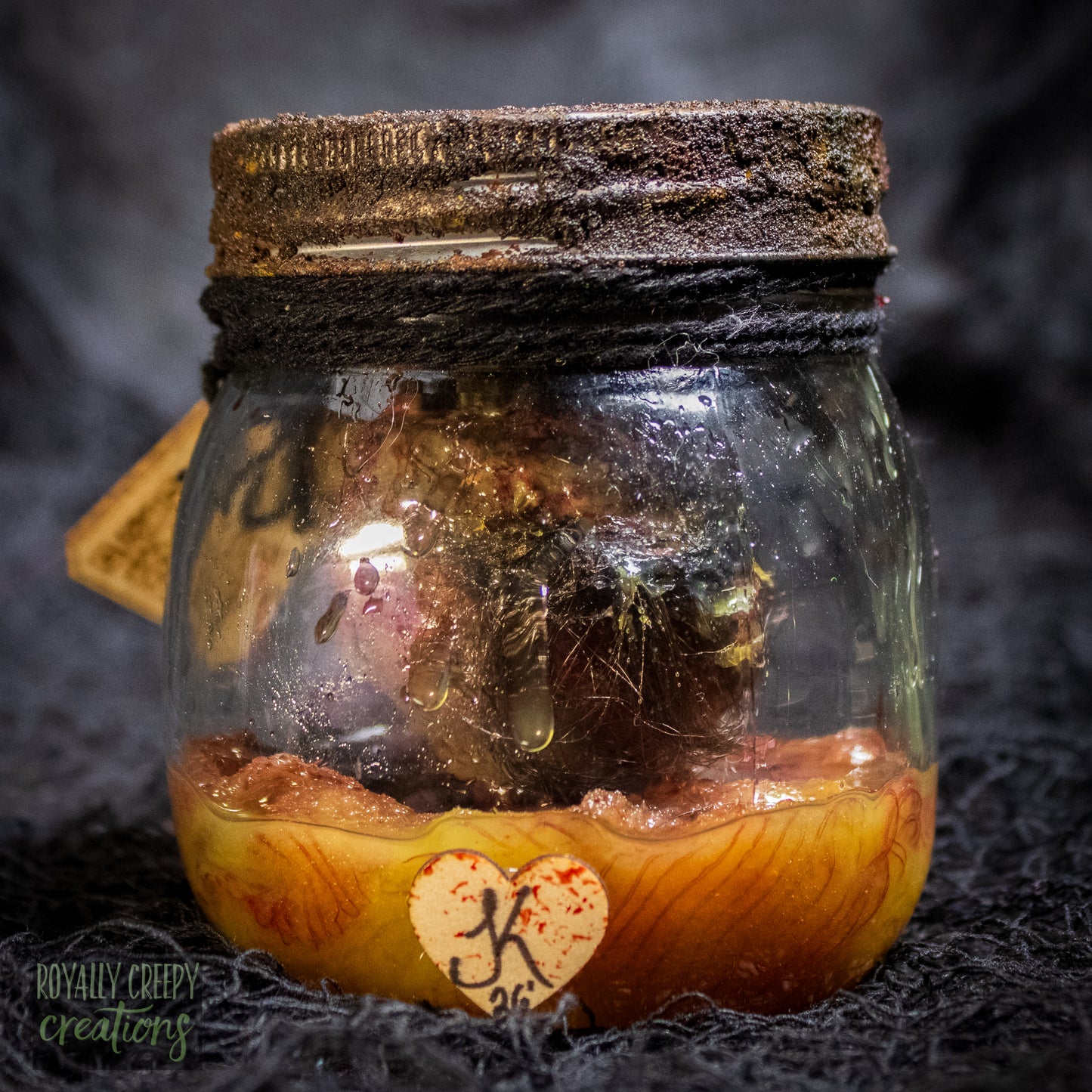 A creepy specimen prop of a severed doll head inside a dirty, rusted glass jar with a dark lid and rope, set against a dark textured background.