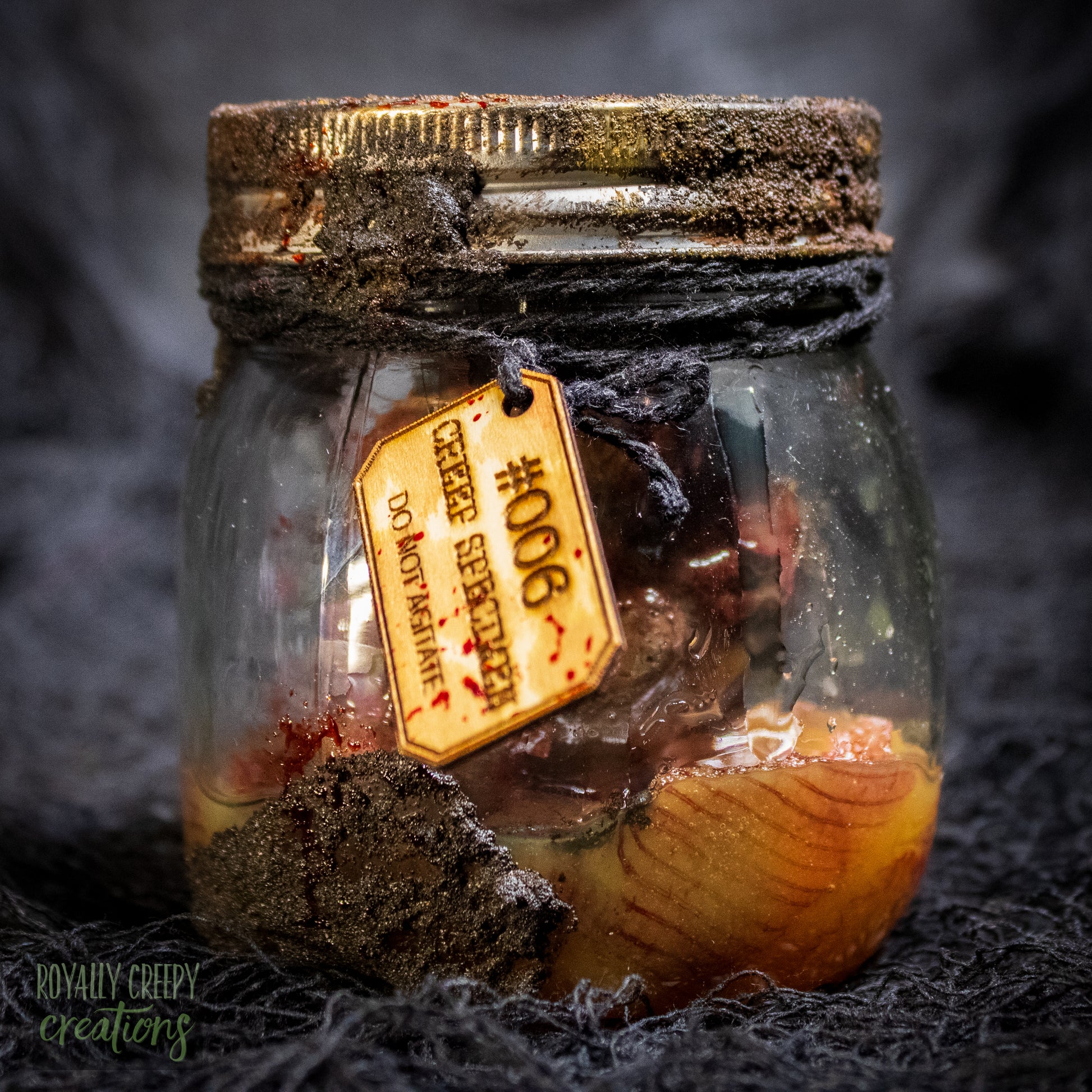 A creepy specimen prop of a severed doll head inside a dirty, rusted glass jar with a dark lid and rope, set against a dark textured background.