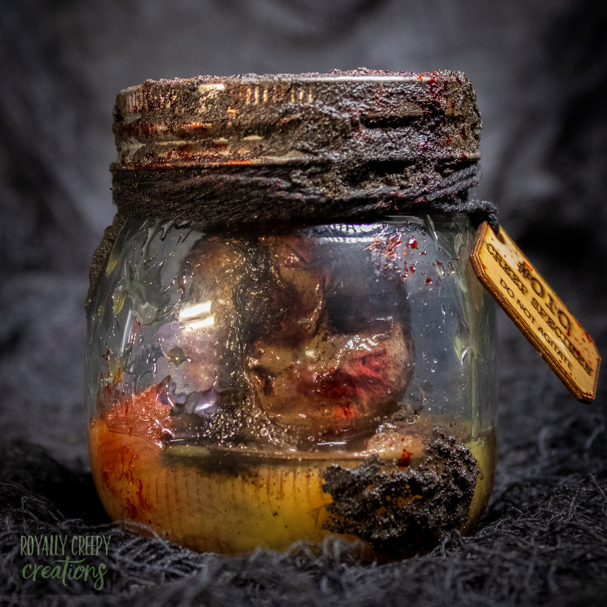A creepy specimen prop of a severed doll head inside a dirty, rusted glass jar with a dark lid and rope, set against a dark textured background.