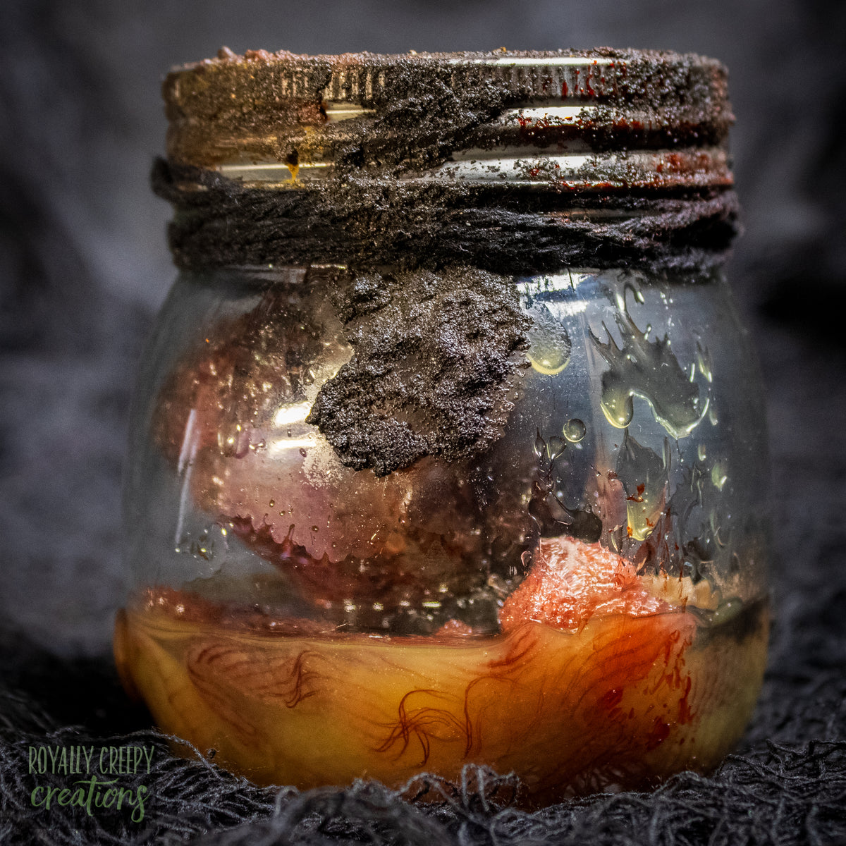 A creepy specimen prop of a severed doll head inside a dirty, rusted glass jar with a dark lid and rope, set against a dark textured background.
