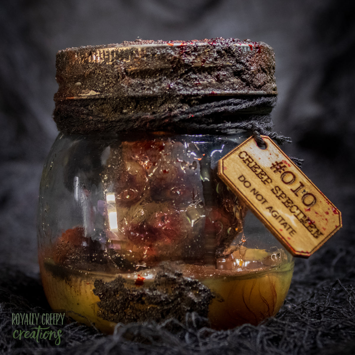 A creepy specimen prop of a severed doll head inside a dirty, rusted glass jar with a dark lid and rope, set against a dark textured background.