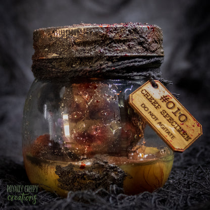 A creepy specimen prop of a severed doll head inside a dirty, rusted glass jar with a dark lid and rope, set against a dark textured background.