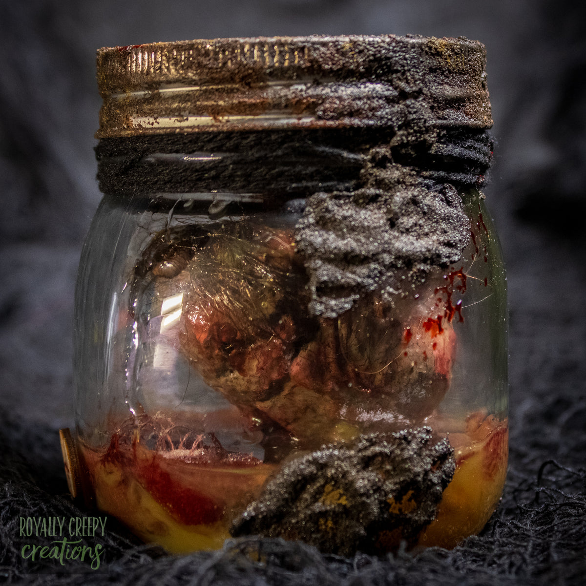A creepy specimen prop of a severed doll head inside a dirty, rusted glass jar with a dark lid and rope, set against a dark textured background.