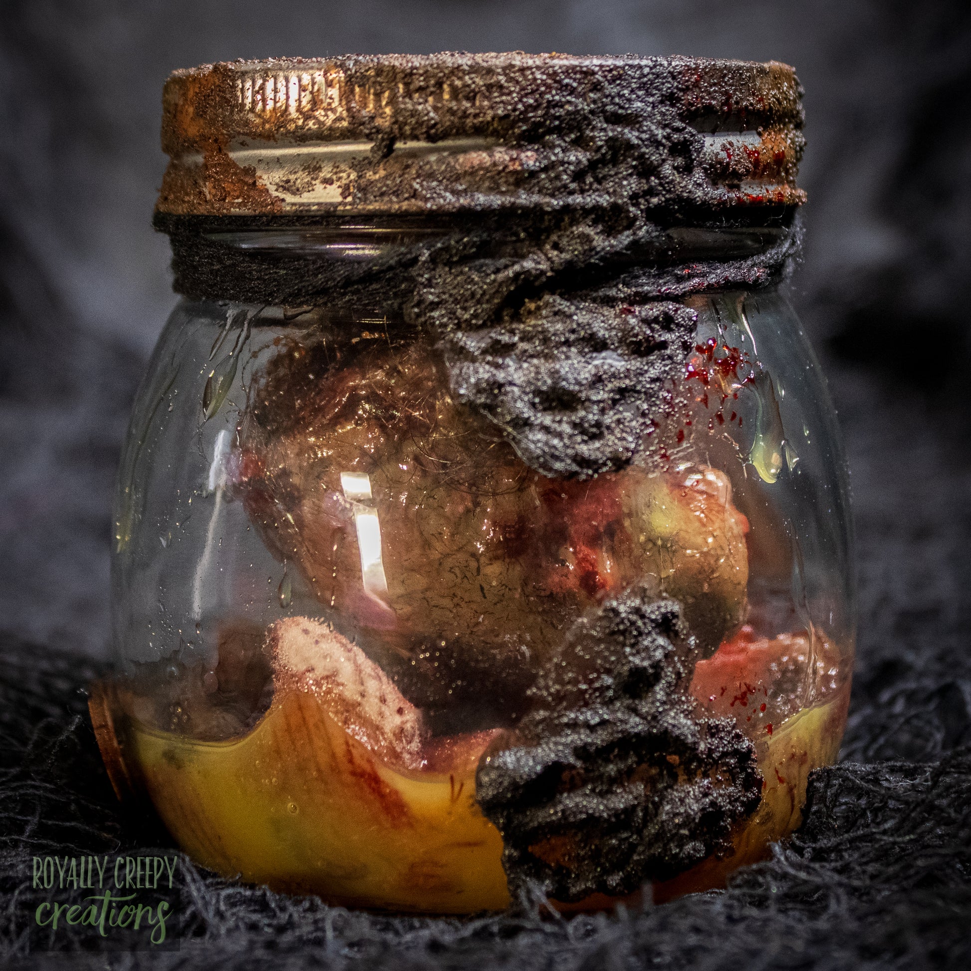 A creepy specimen prop of a severed doll head inside a dirty, rusted glass jar with a dark lid and rope, set against a dark textured background.