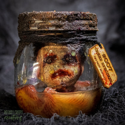 A creepy specimen prop of a severed doll head inside a dirty, rusted glass jar with a dark lid and rope, set against a dark textured background.