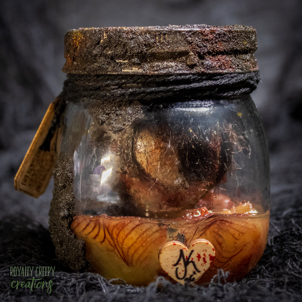 A creepy specimen prop of a severed doll head inside a dirty, rusted glass jar with a dark lid and rope, set against a dark textured background.