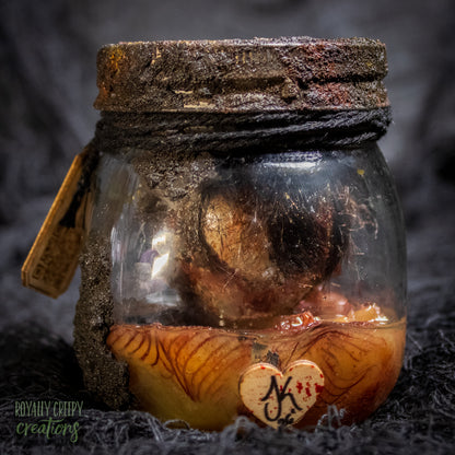 A creepy specimen prop of a severed doll head inside a dirty, rusted glass jar with a dark lid and rope, set against a dark textured background.
