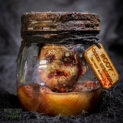 A creepy specimen prop of a severed doll head inside a dirty, rusted glass jar with a dark lid and rope, set against a dark textured background.