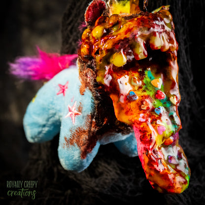 A creepy, horror-themed keychain featuring a plush unicorn vomiting up a rainbow.