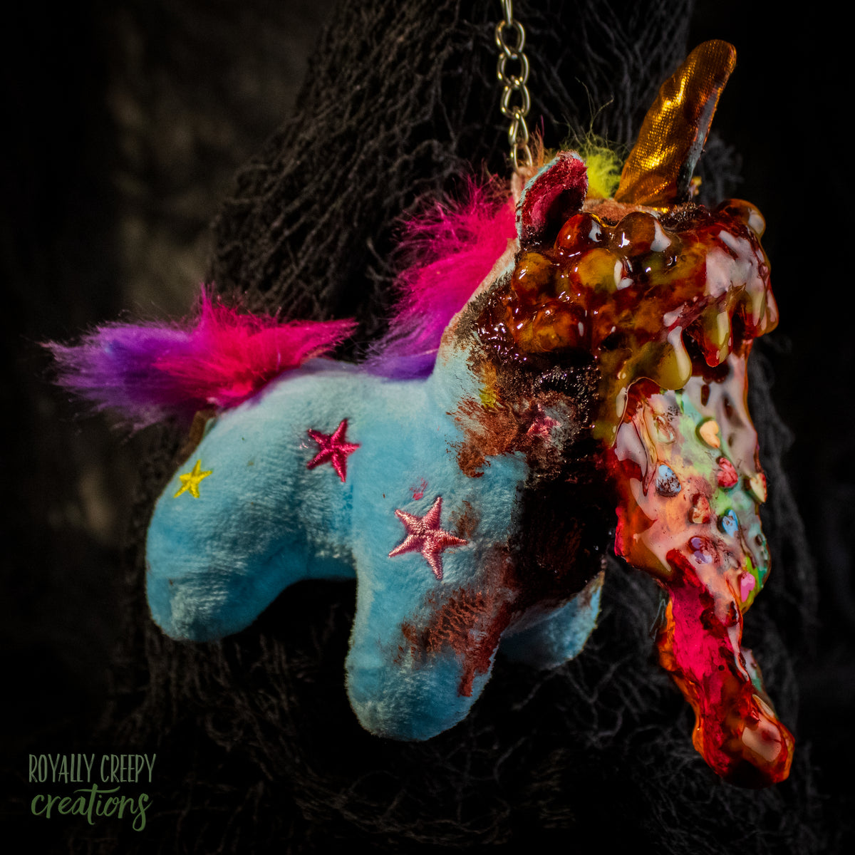 A creepy, horror-themed keychain featuring a plush unicorn vomiting up a rainbow.