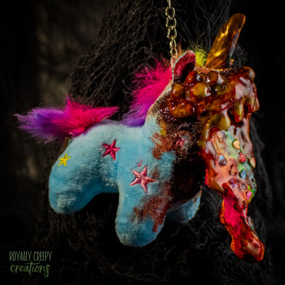 A creepy, horror-themed keychain featuring a plush unicorn vomiting up a rainbow.
