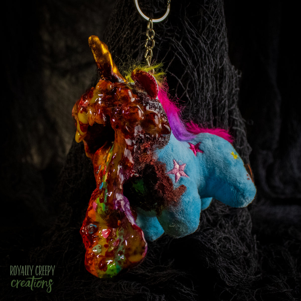 A creepy, horror-themed keychain featuring a plush unicorn vomiting up a rainbow.