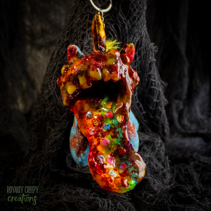 A creepy, horror-themed keychain featuring a plush unicorn vomiting up a rainbow.
