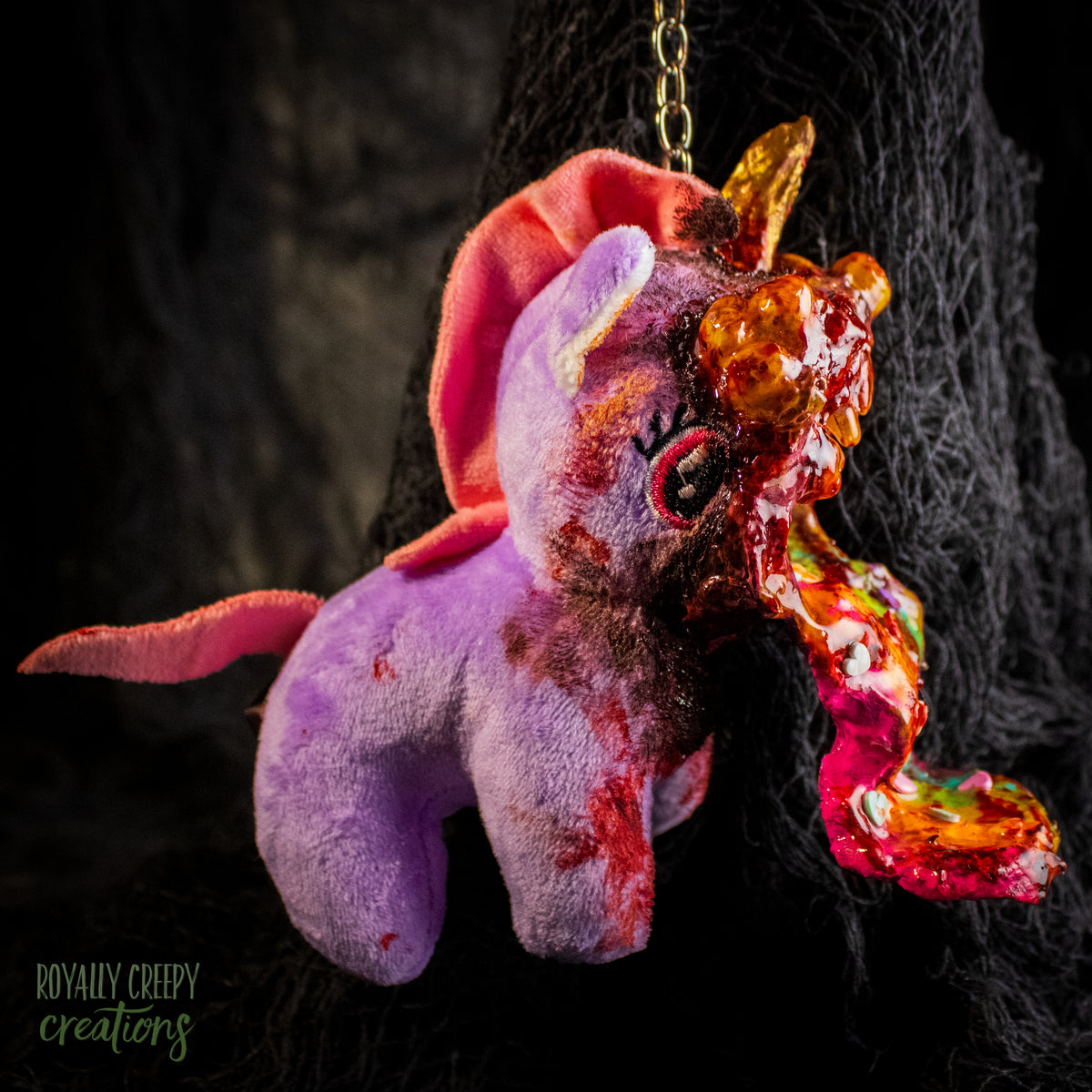 A creepy, horror-themed keychain featuring a plush unicorn vomiting up a rainbow.