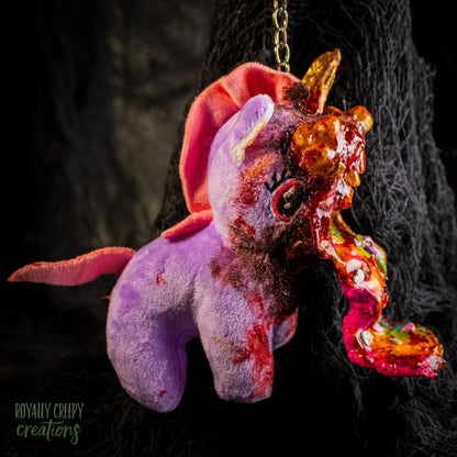 A creepy, horror-themed keychain featuring a plush unicorn vomiting up a rainbow.
