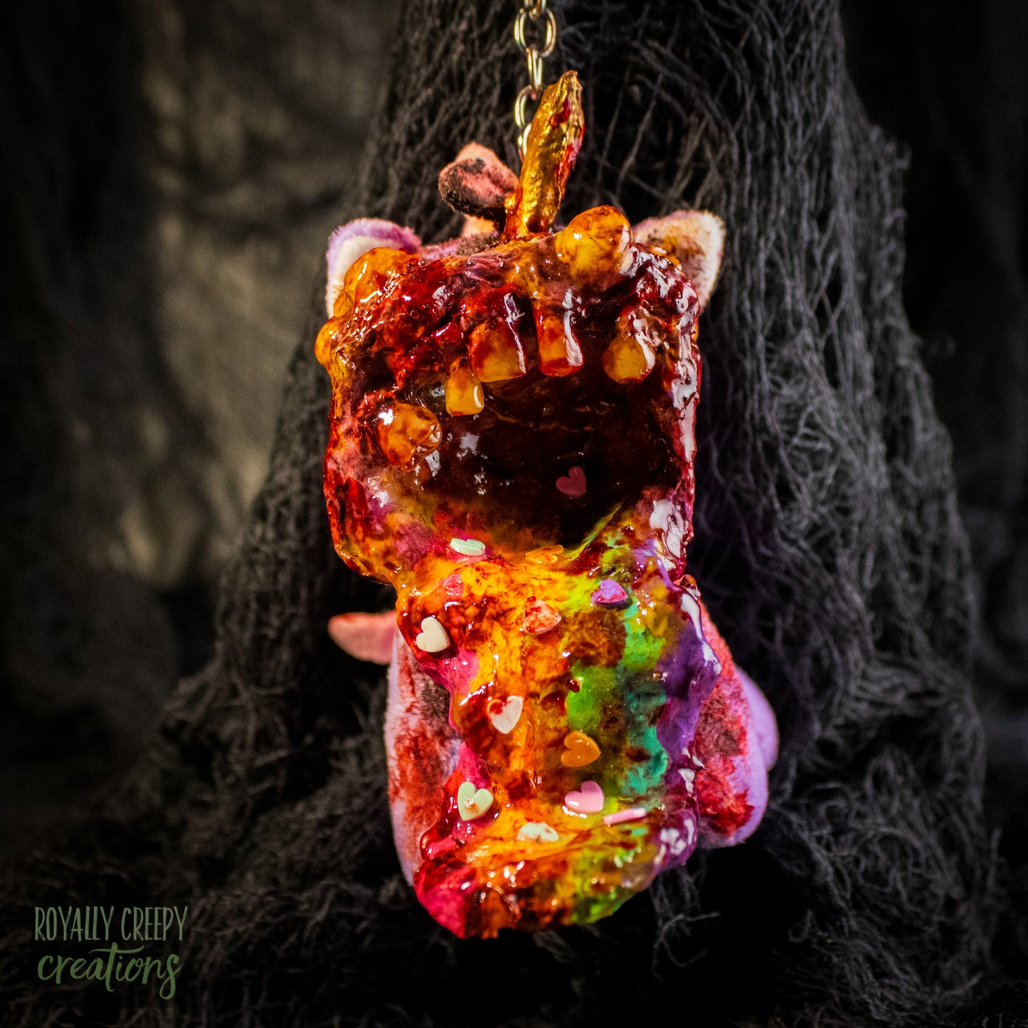 A creepy, horror-themed keychain featuring a plush unicorn vomiting up a rainbow.