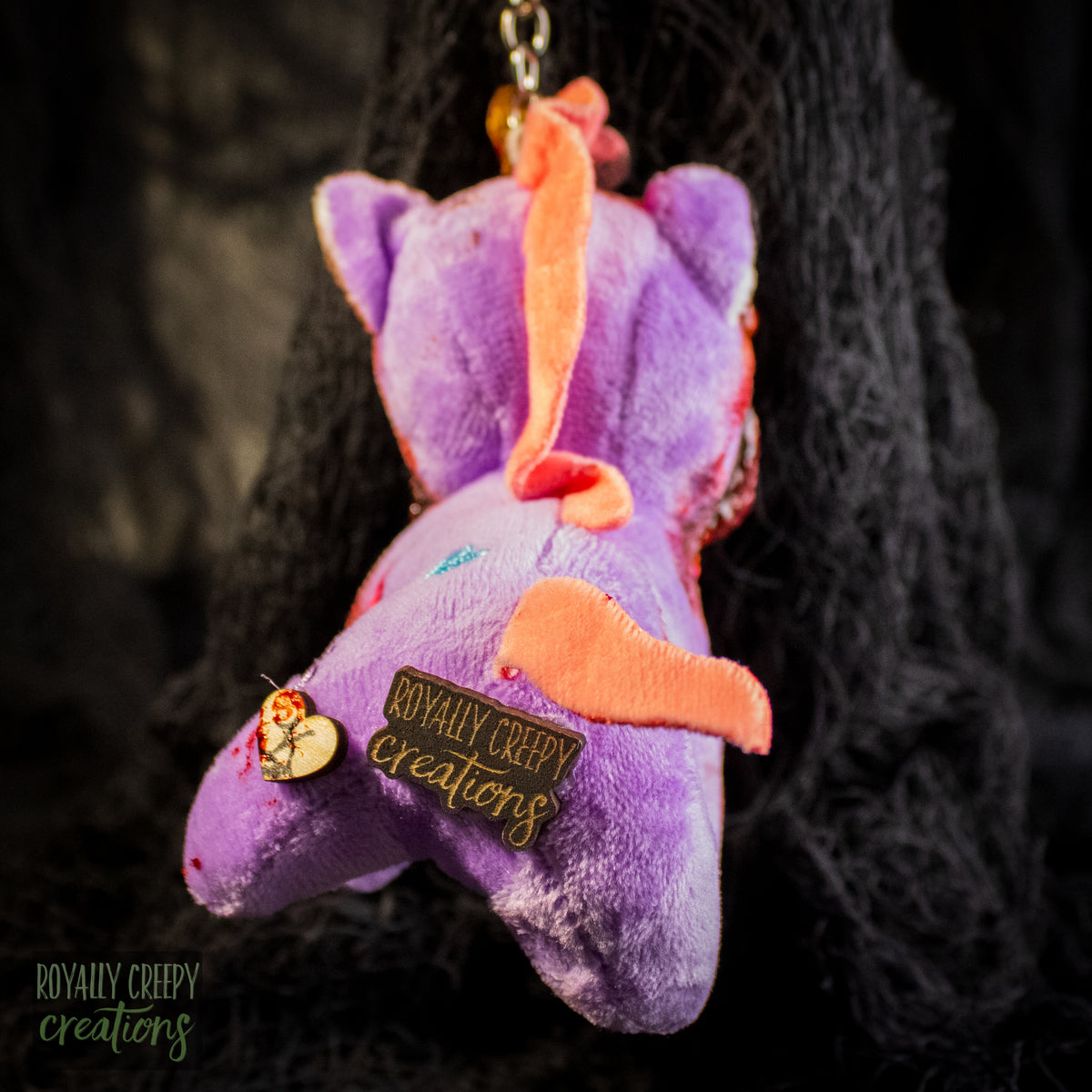 Back view of a purple plush unicorn keychain a tag that reads 'ROYALLY CREEPY creations'.