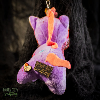 Back view of a purple plush unicorn keychain a tag that reads 'ROYALLY CREEPY creations'.